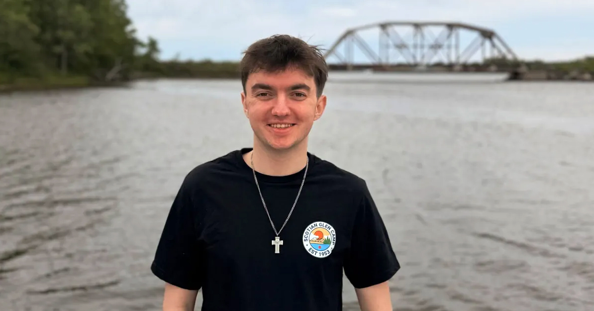A young man standing by a body of water with a bridge in the background